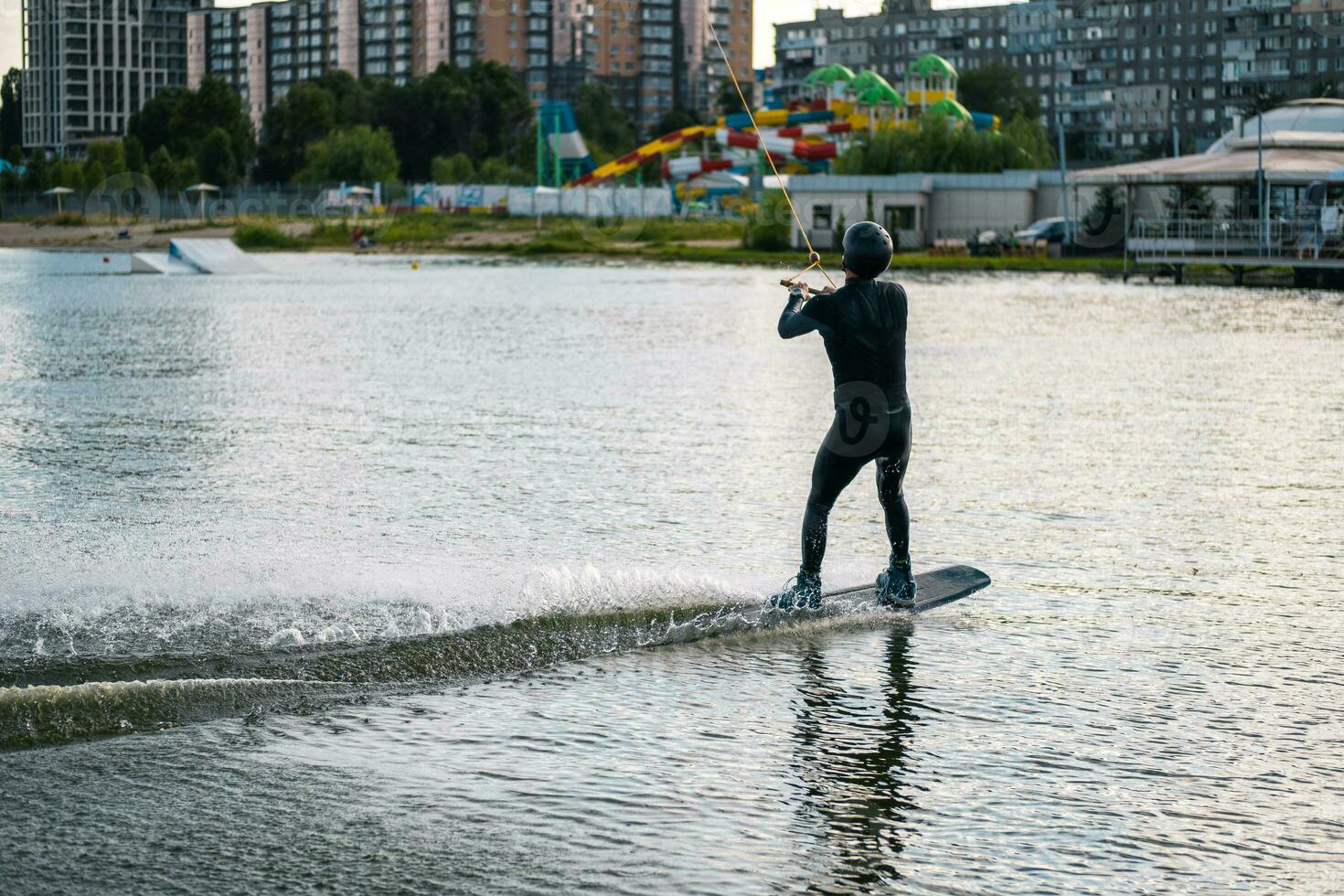 Sporty man balancing on wakeboard, riding on calm water of river on sunny day photo