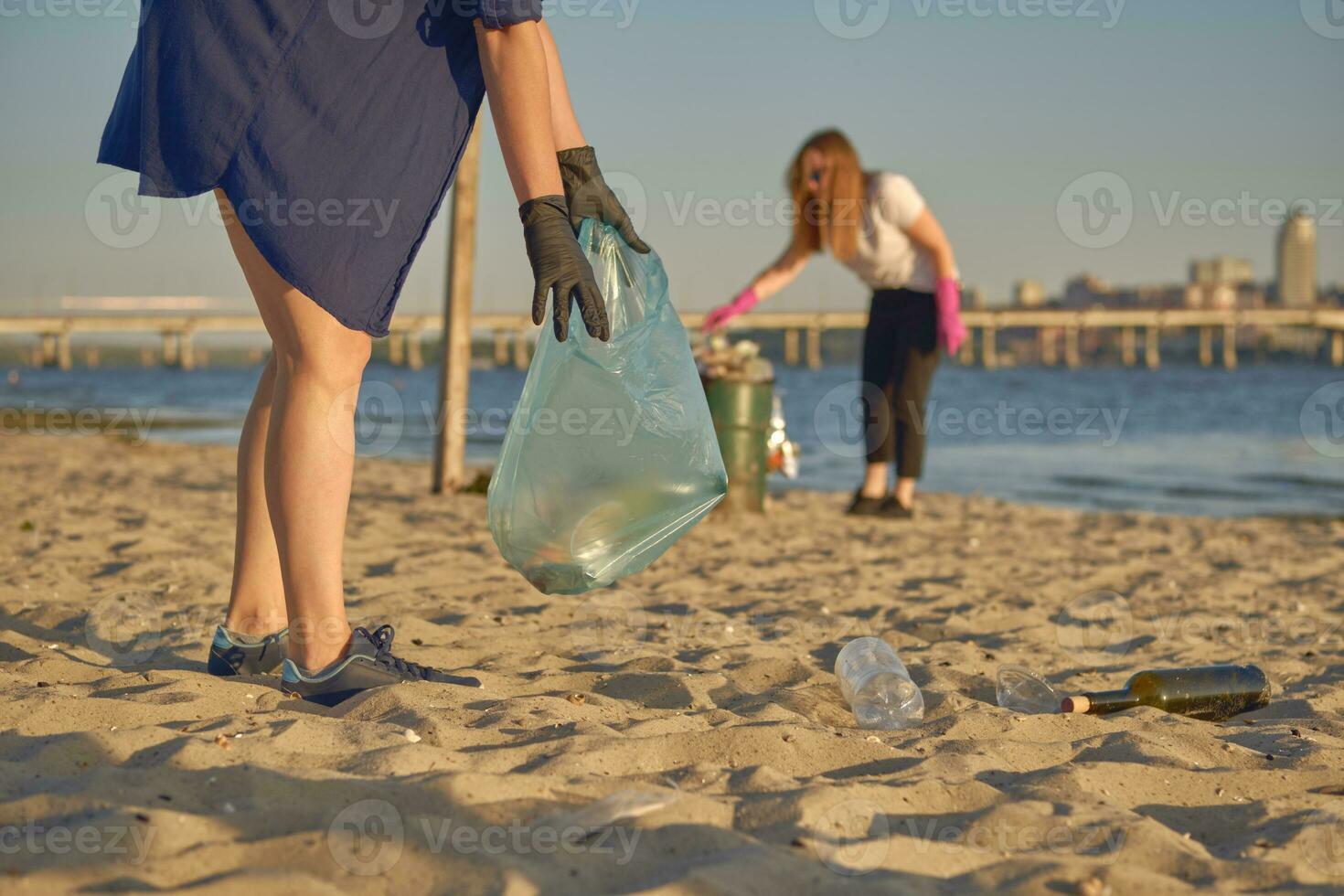 Young volunteers in black gloves are walking with garbage bags along a dirty beach of the river and cleaning up trash. People and ecology. Close-up. photo