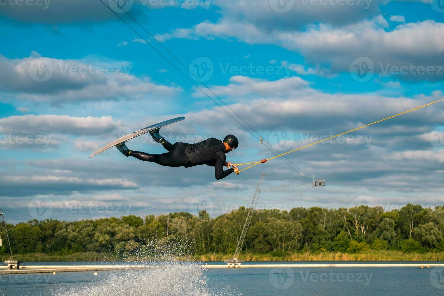 Athletic man practicing wakeboard tricks in training wake park on summer day photo