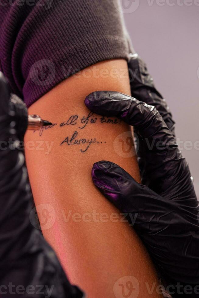 Hands of professional tattoo artist creating inscriptions on arm of woman photo