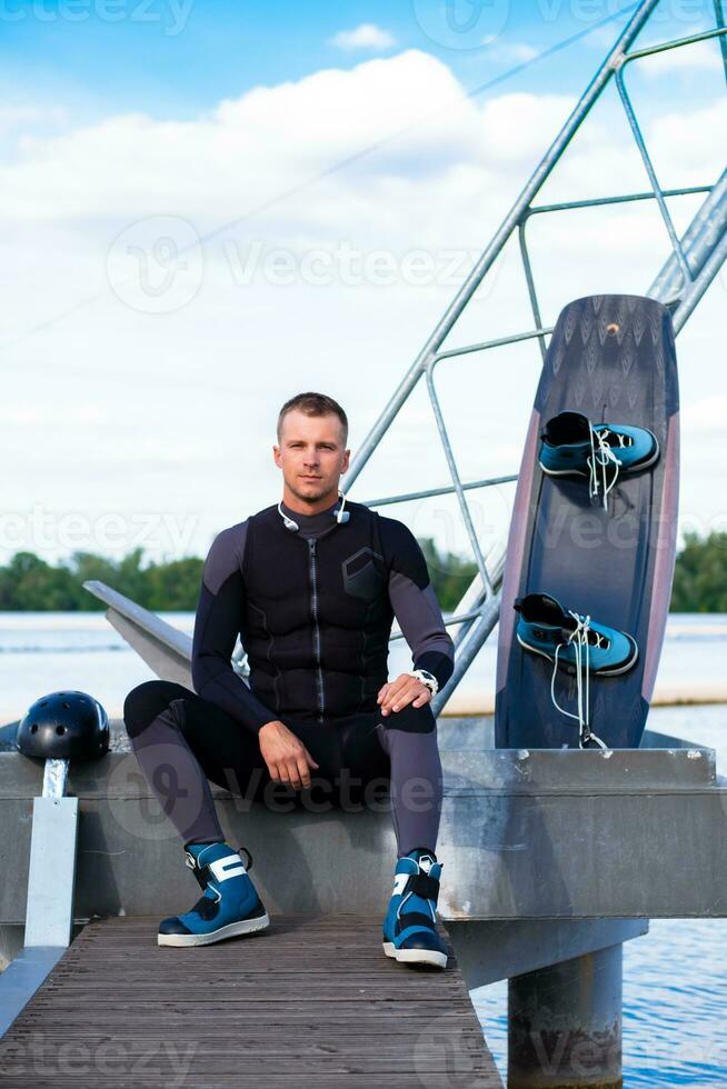 Confident wakeboarder sitting on pier with wakeboard, preparing for training photo