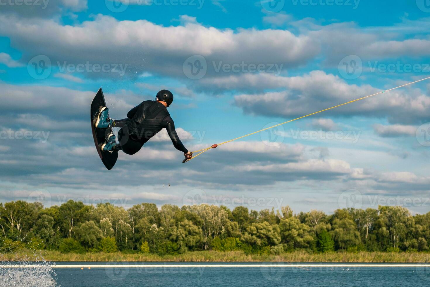 Experienced wakeboard rider towed on cable jumping and spinning in air in open water photo
