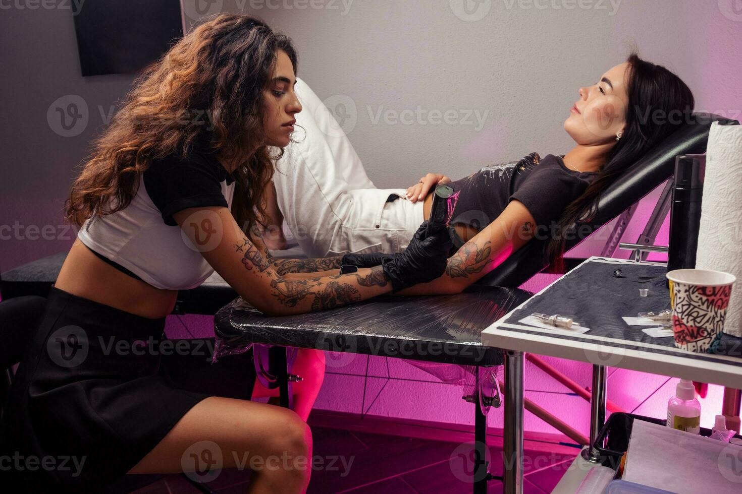 Female tattoo artist making colorful tattoo for girl in salon photo