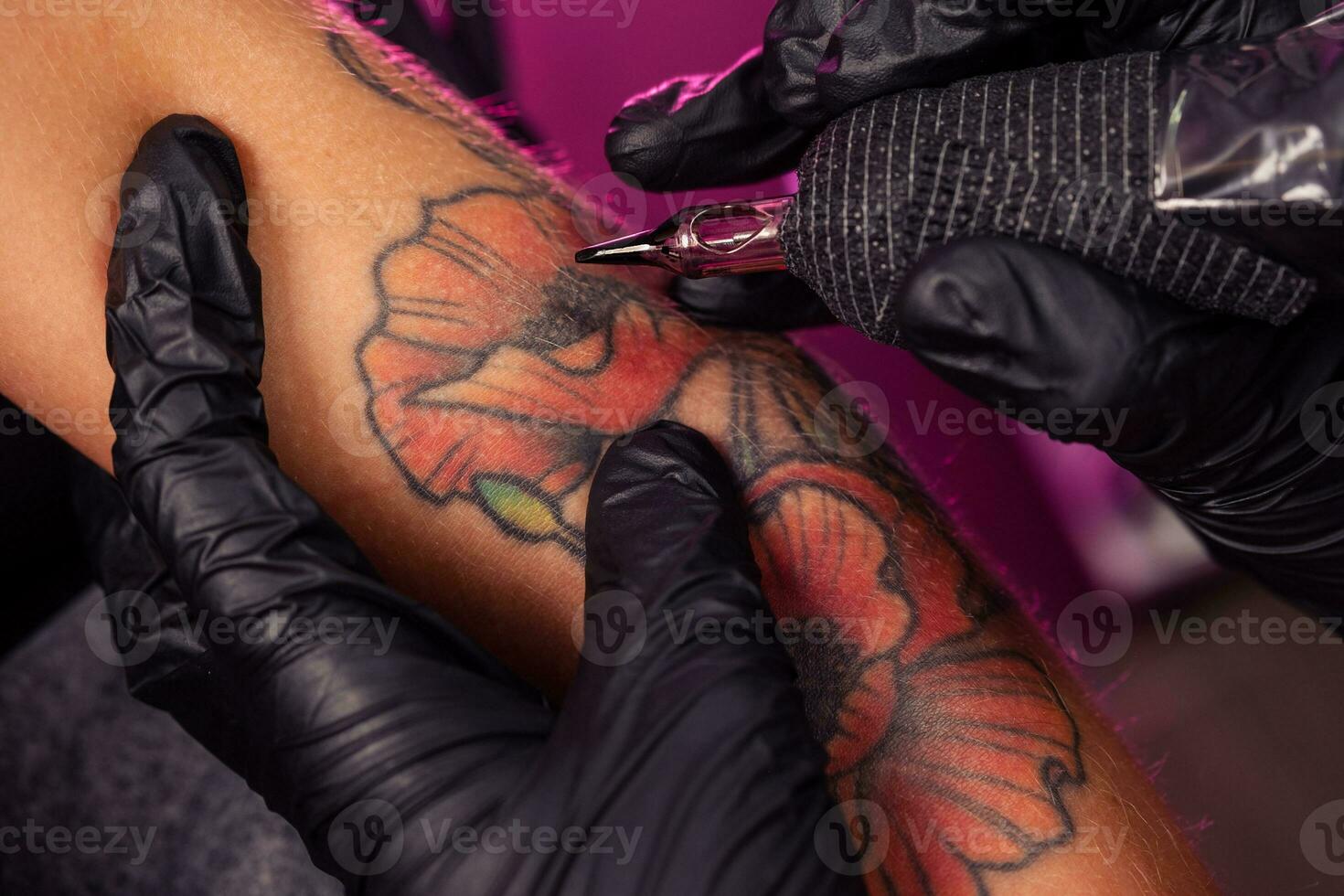 Tattoo artist using machine to ink colorful poppy onto womans hand photo