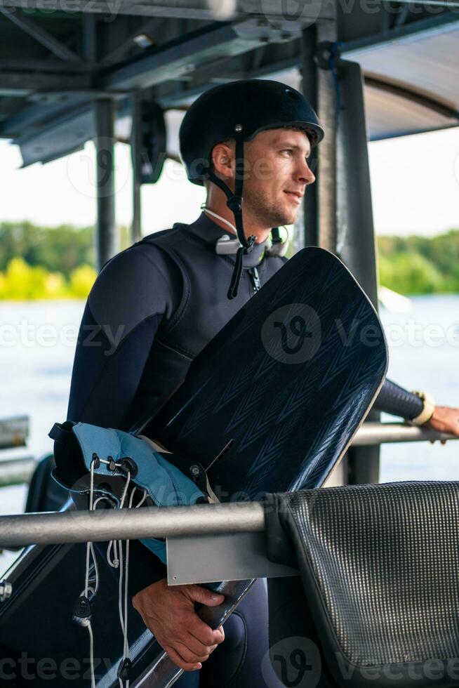 Confident smiling wakeboarder in full gear with board staning on start dock photo