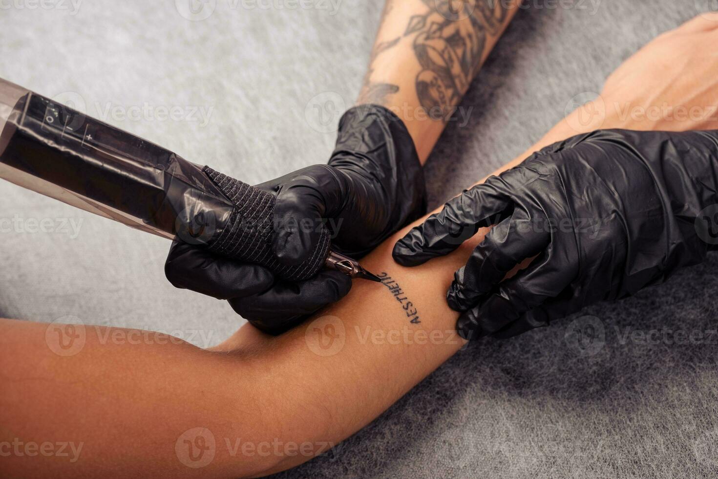 Hands of tattoo artist tattooing word AESTHETIC on client forearm photo