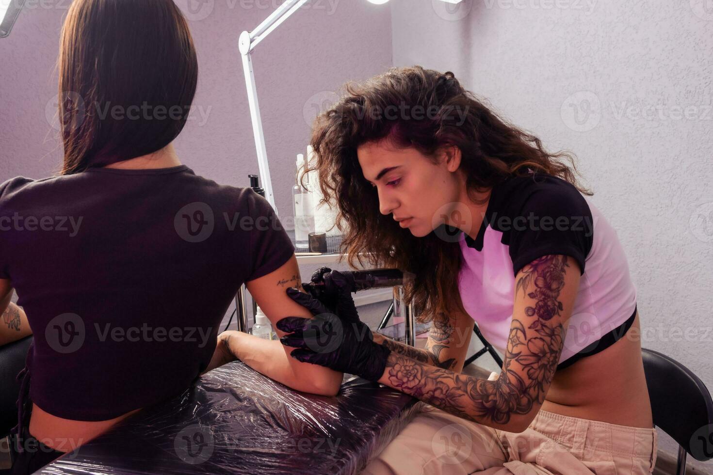 Professional female tattooer creating lettering design on arm of client photo