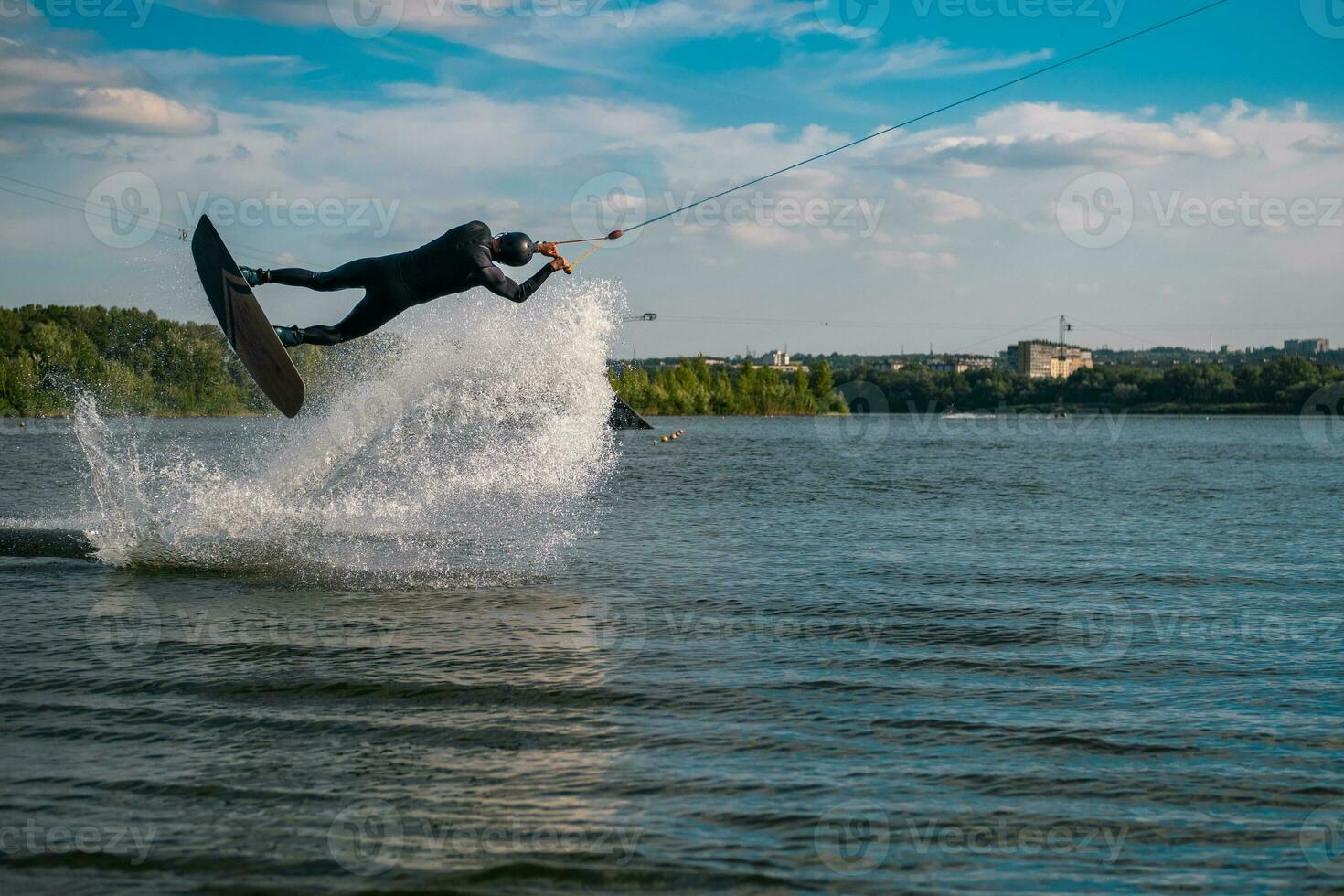 Wakeboarder practicing tricks jumping on board above water surface creating splashes photo