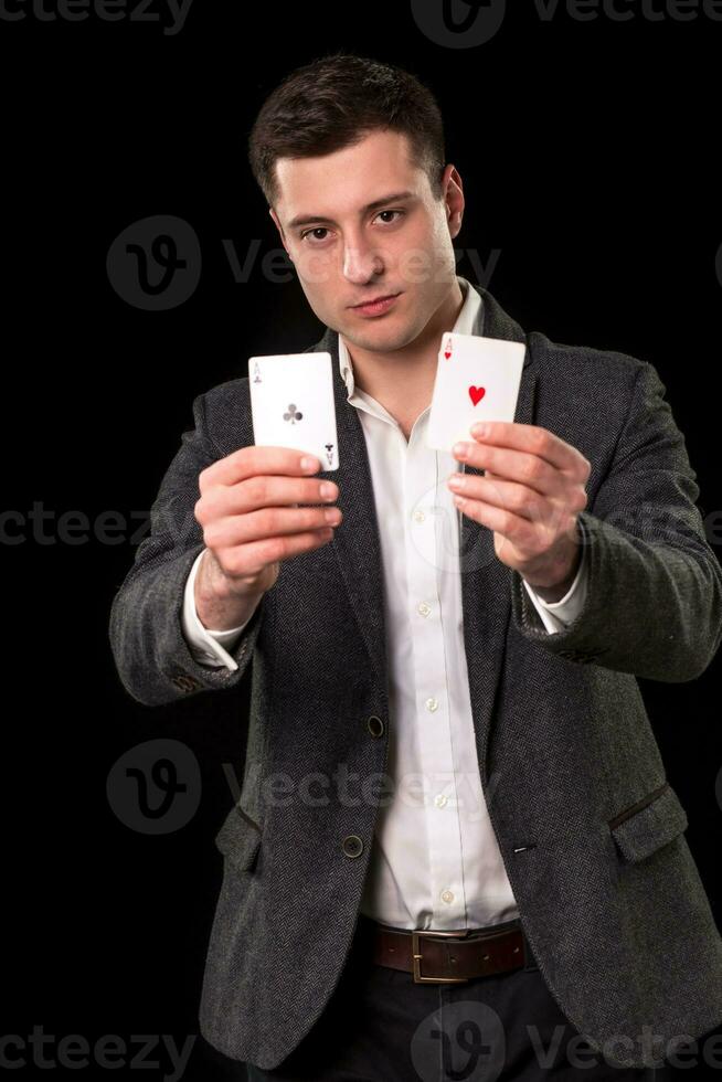 Young caucasian man wearing suit holding two aces in his hands on black background. Gambling concept. Casino photo