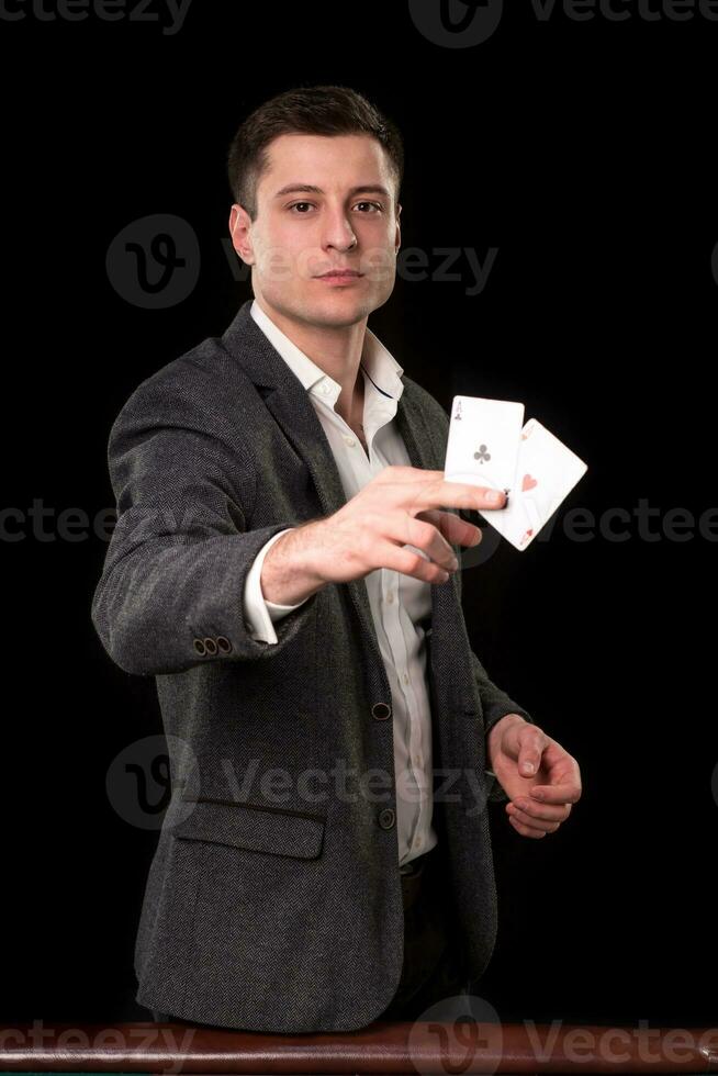 Young caucasian man wearing suit holding two aces in his hand on black background. Gambling concept. Casino photo