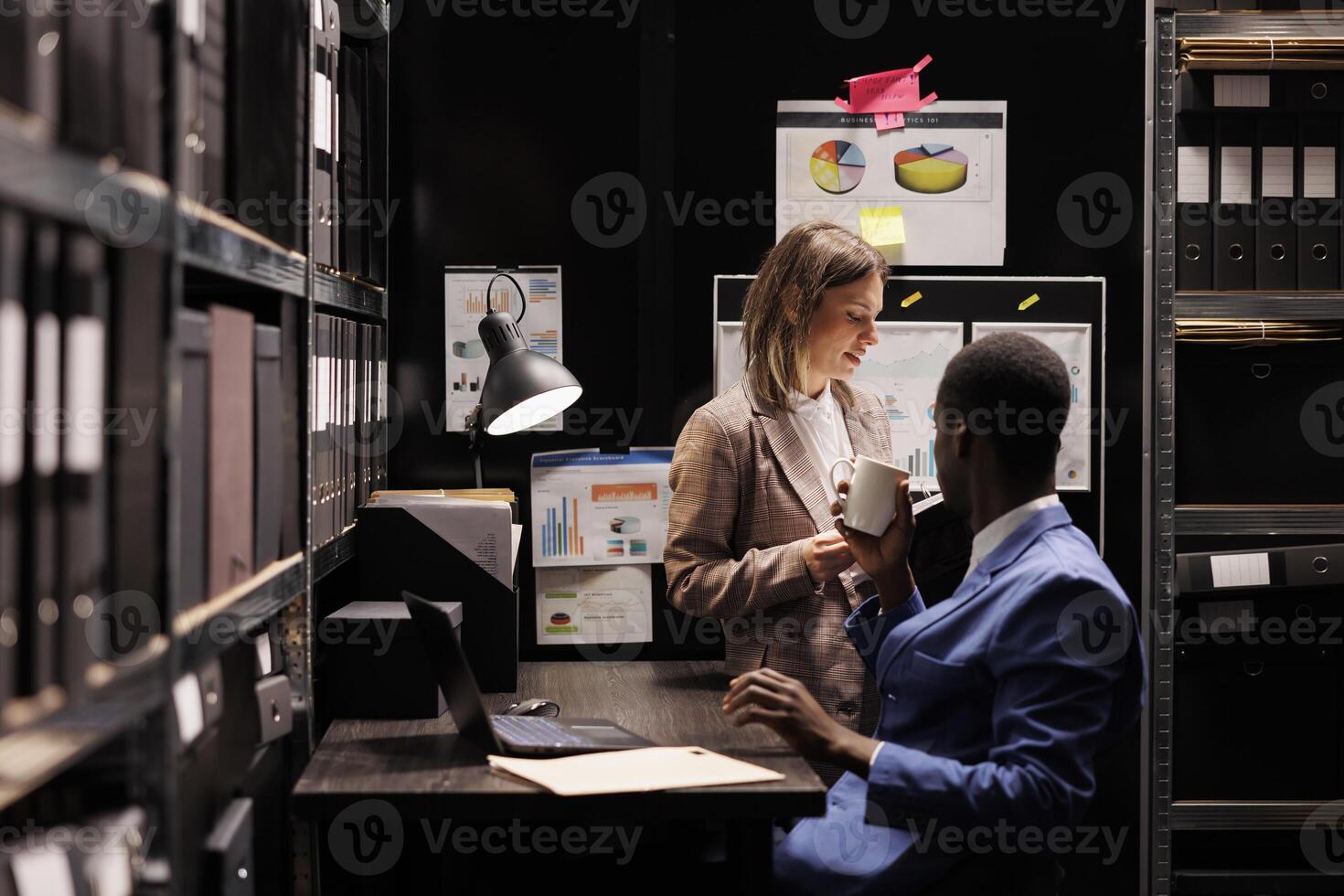 Managers checking accountancy report, working late at night at administrative record in corporate depository. Diverse businesspeople discussing bookkeeping documents in storage room. photo