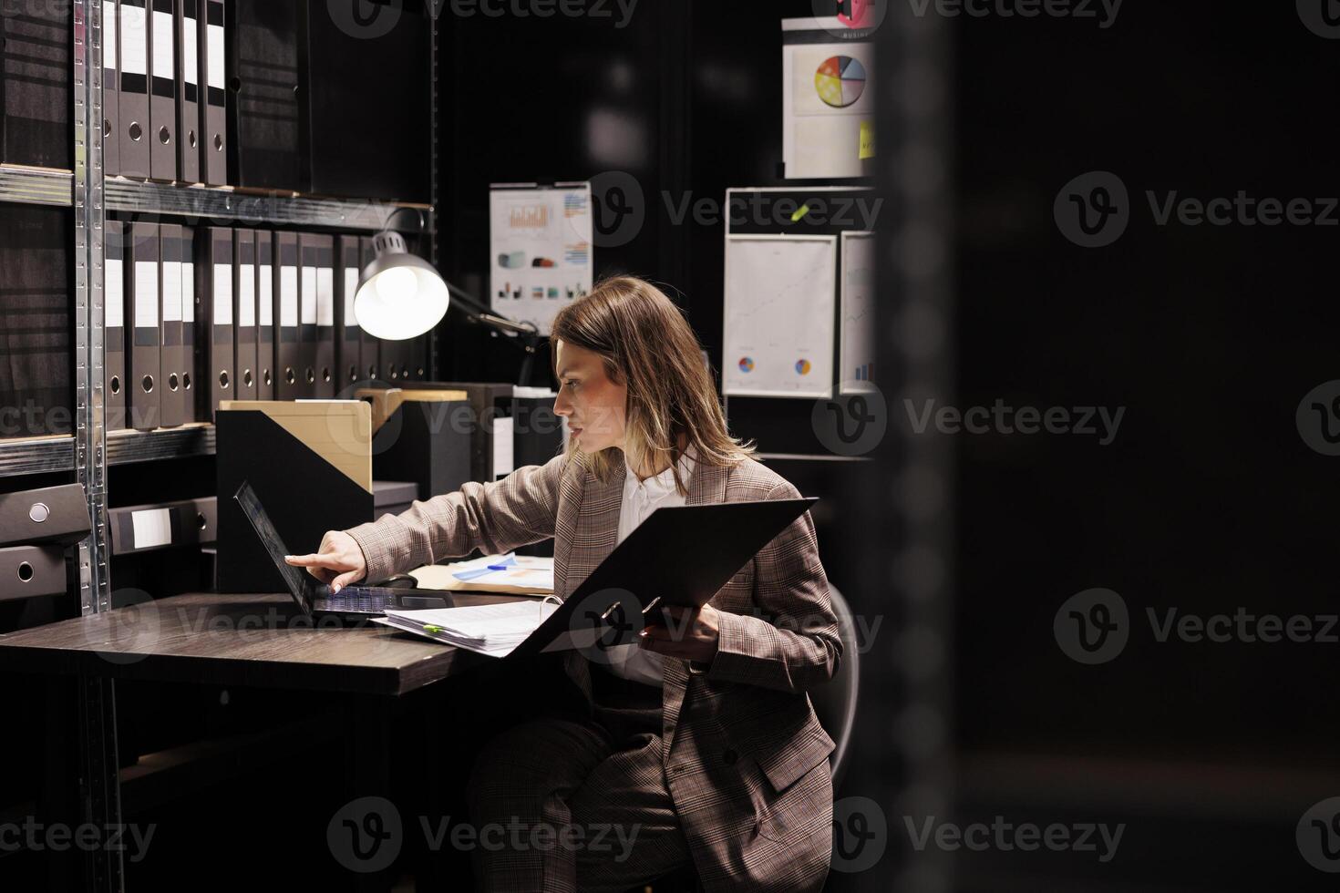 Investigator reading criminology files, working late at night at criminal case in arhive room. Police officer analyzing crime scene evidence, checking documents with confidential victim information photo