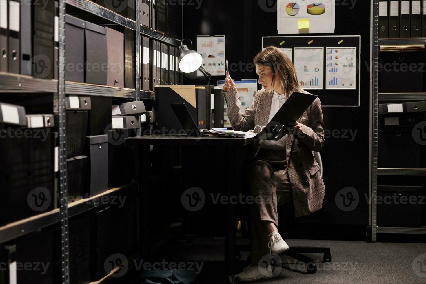 inspector leyendo policía informe, trabajando tarde a noche a delincuente caso en archivar habitación. privado detective analizando crimen escena evidencia, molesto a captura misterioso sospechar. ley aplicación concepto foto