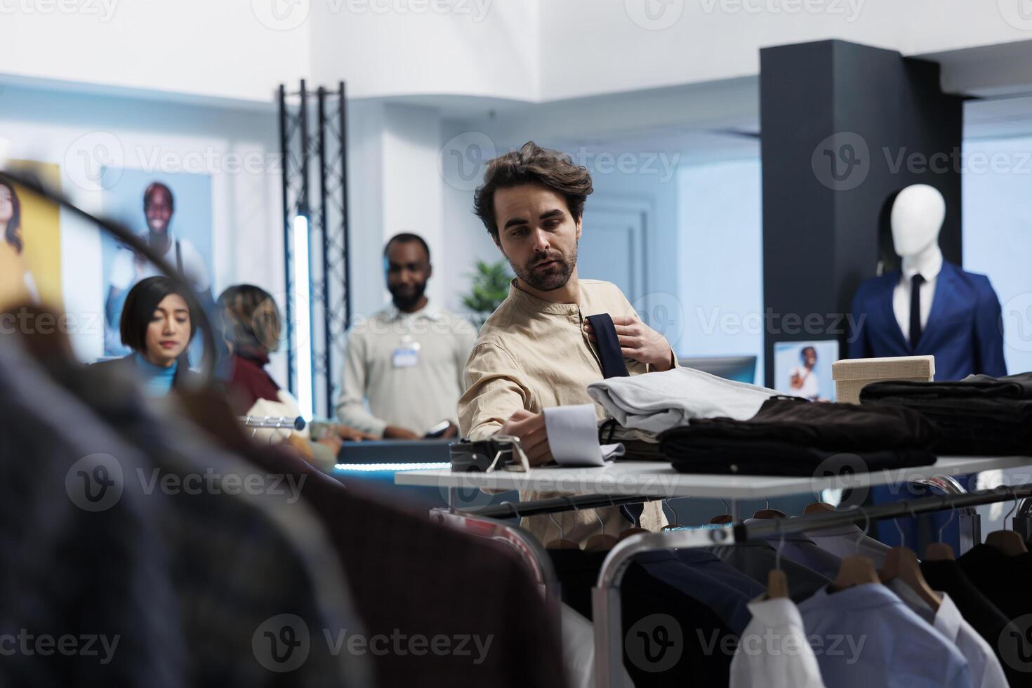 Young man choosing stylish tie and examining options while shopping in clothing store. Fashion boutique customer selecting formal trendy accessory in menswear retail department photo