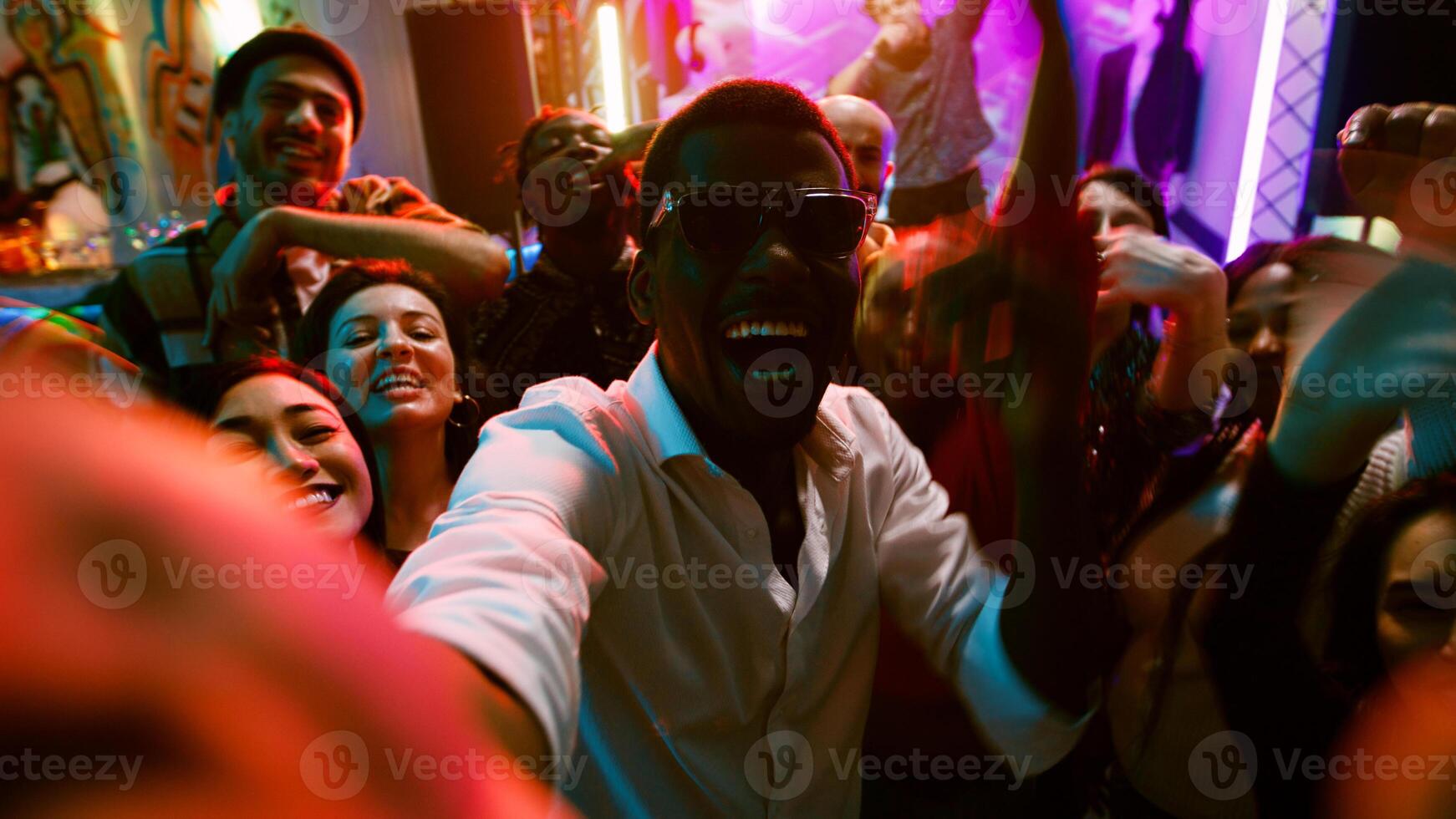 POV of funky people filming video at party, making memories on dance floor with friends at nightclub. Cheerful persons taking pictures and recording vlog at modern celebration. Handheld shot. photo