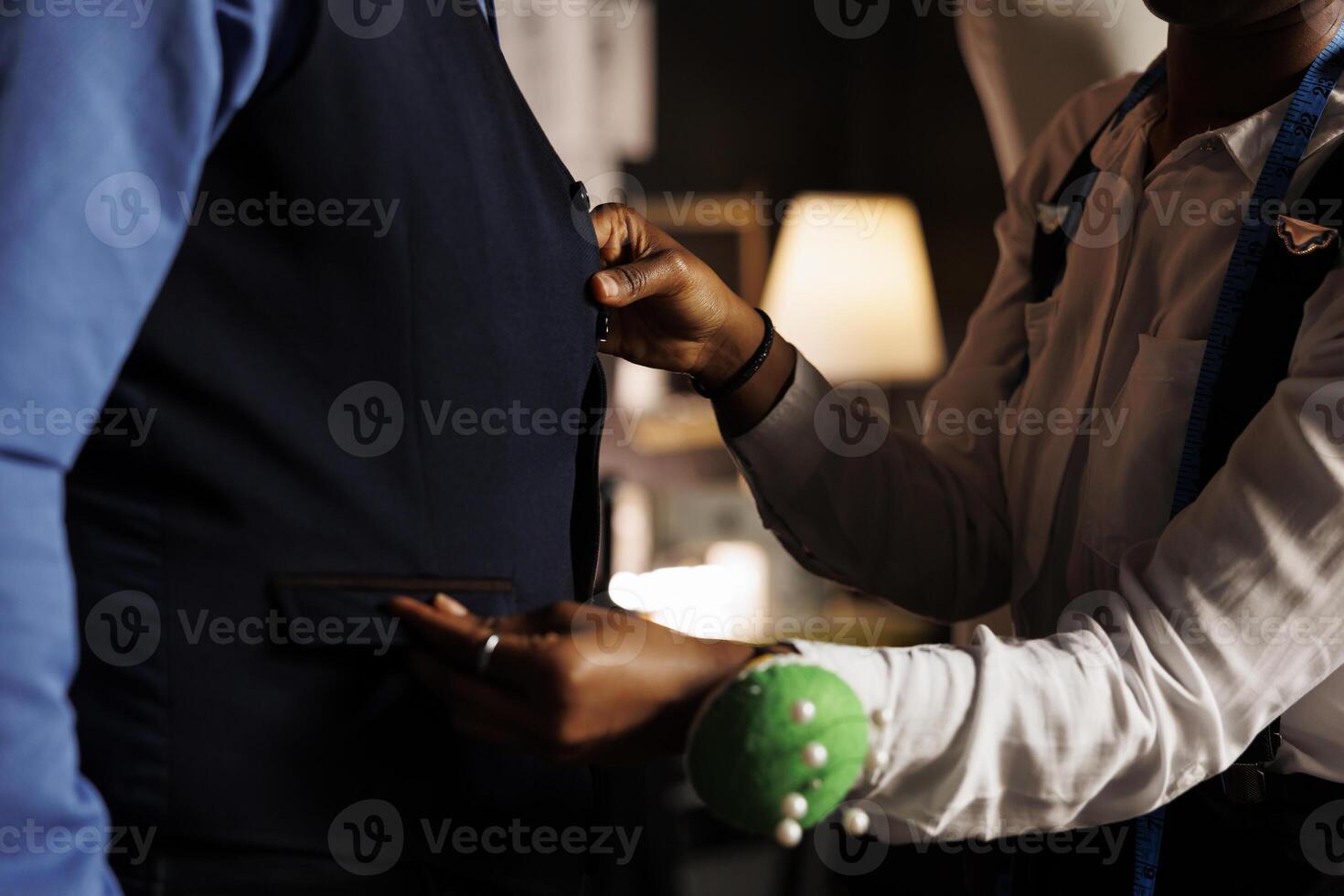 Professional seamstress doing precise needlework on premium quality elegant bespoke costume piece in tailoring studio. Skilled couturier finishing measurements on client comissioned vest, close up photo
