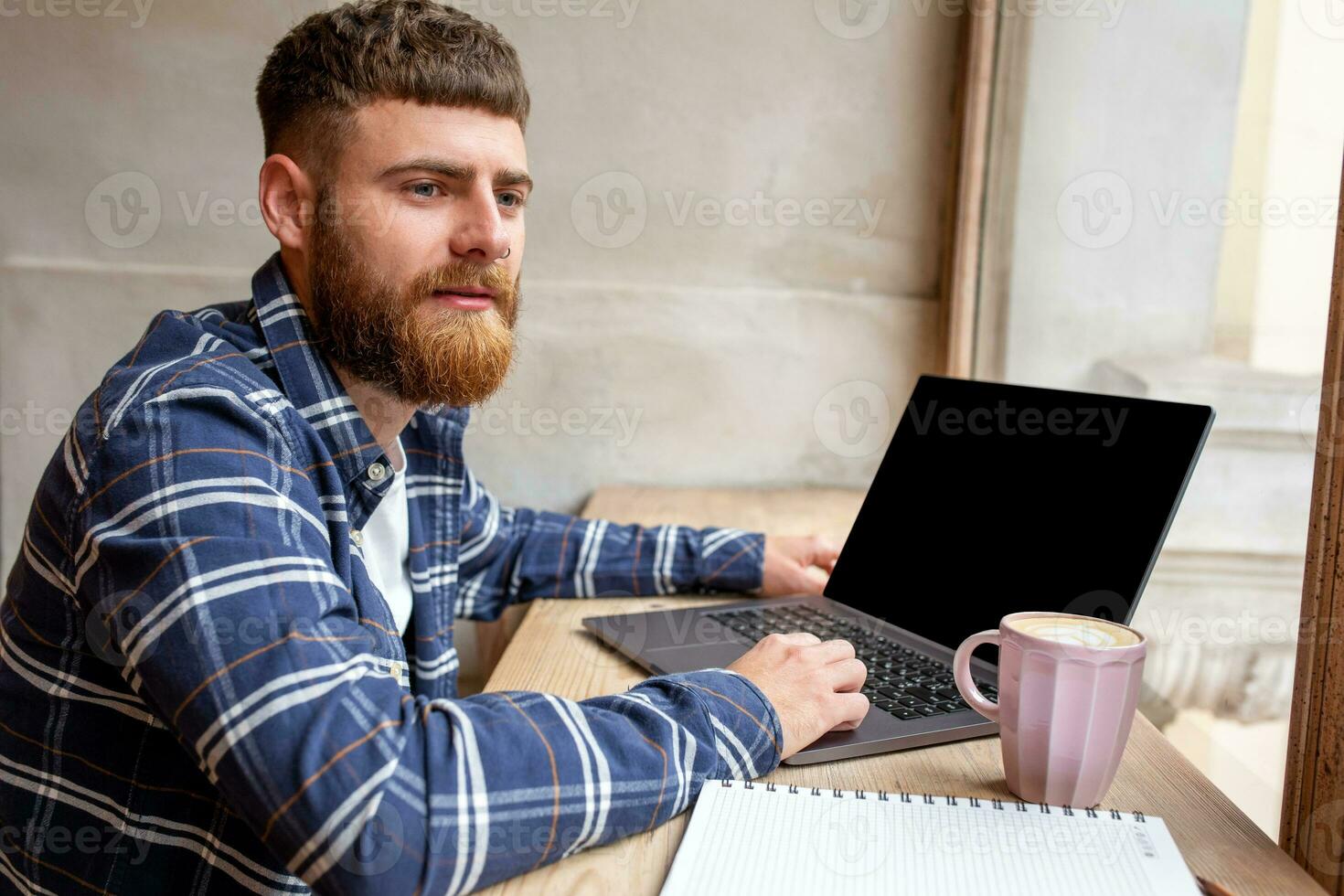 Young man chatting via net-book during work break in coffee shop, male sitting in front open laptop computer with blank copy space screen. photo