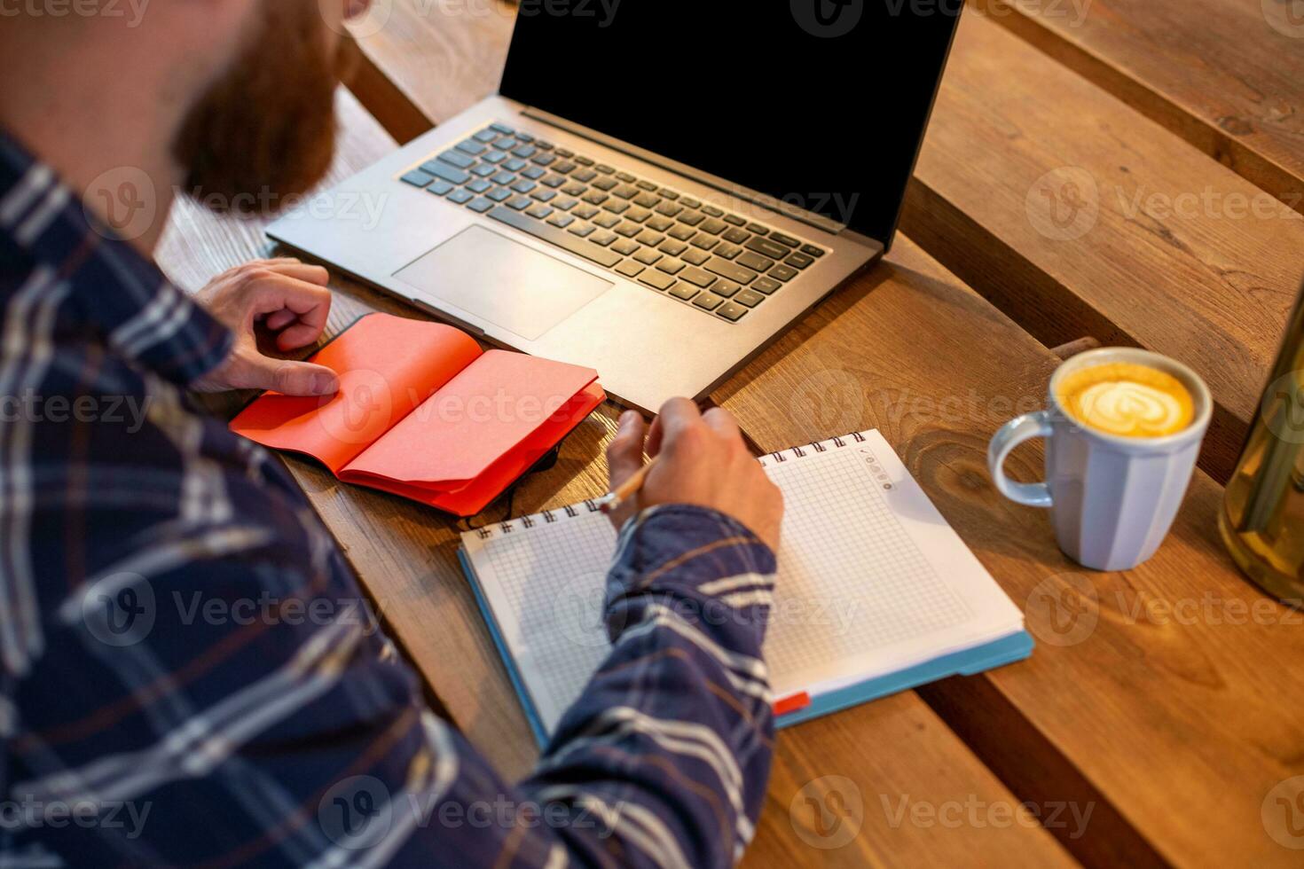 Cropped image of casual business man or freelancer planning his work on notebook, working on laptop computer with smart phone, cup of coffee on table at coffee shop or home office. photo