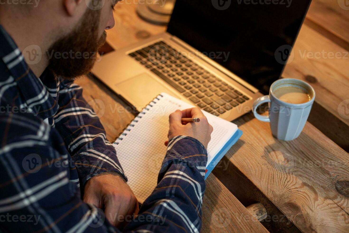 Cropped image of casual business man or freelancer planning his work on notebook, working on laptop computer with smart phone, cup of coffee on table at coffee shop or home office. photo