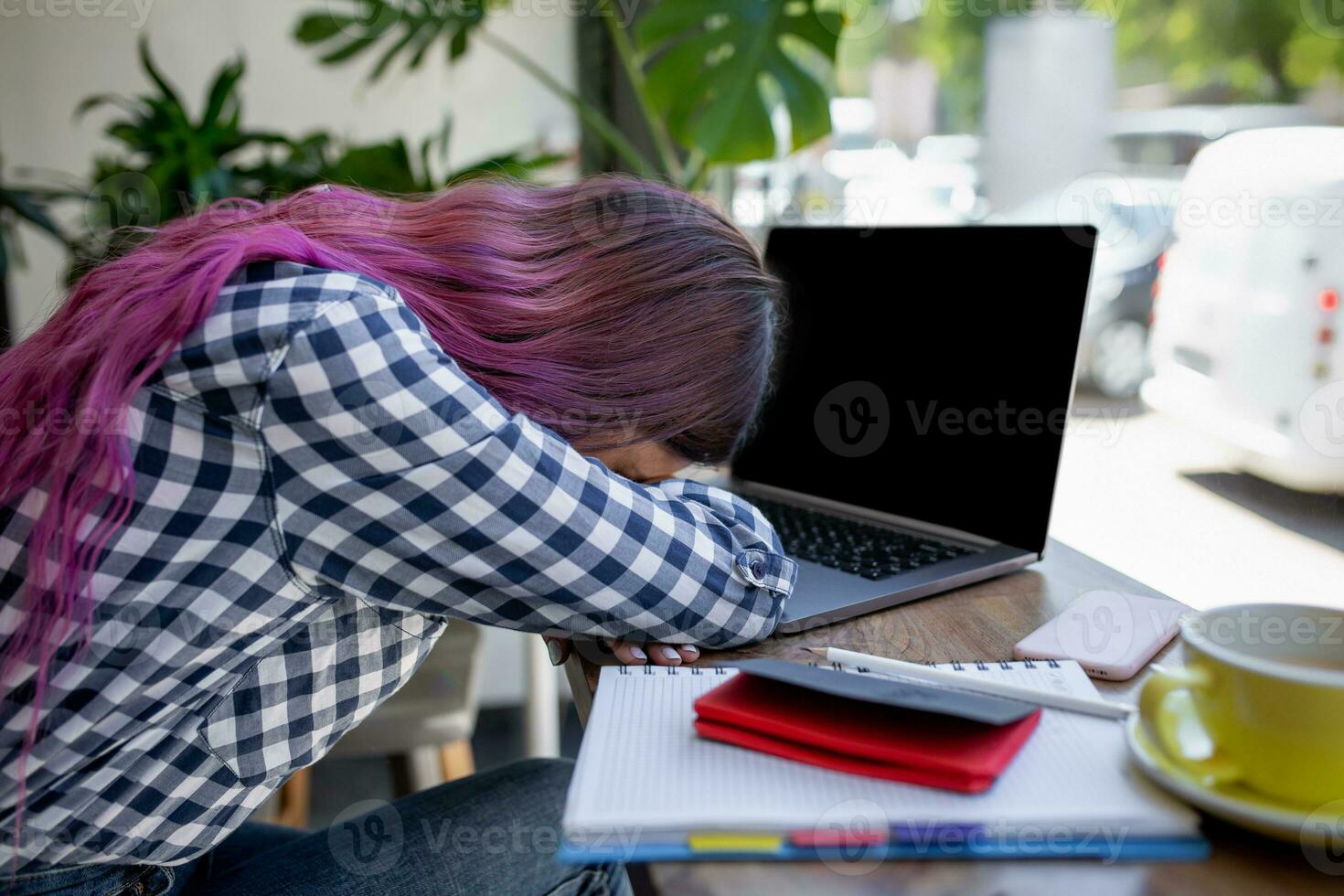 Young woman lying on her arms on the table in cafe in front of laptop with cup of coffee, sleepy. photo