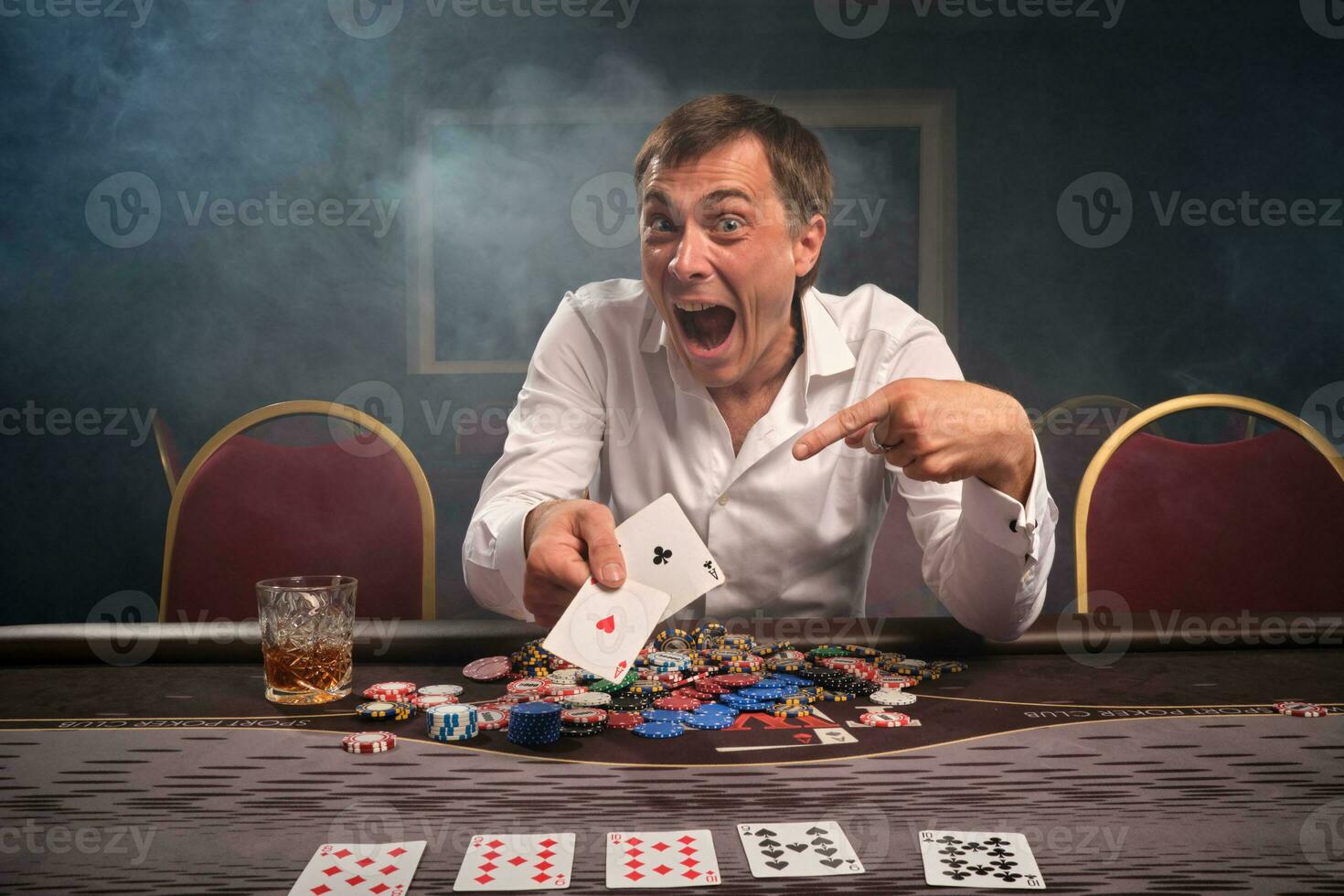 Handsome emotional man is playing poker sitting at the table in casino. photo