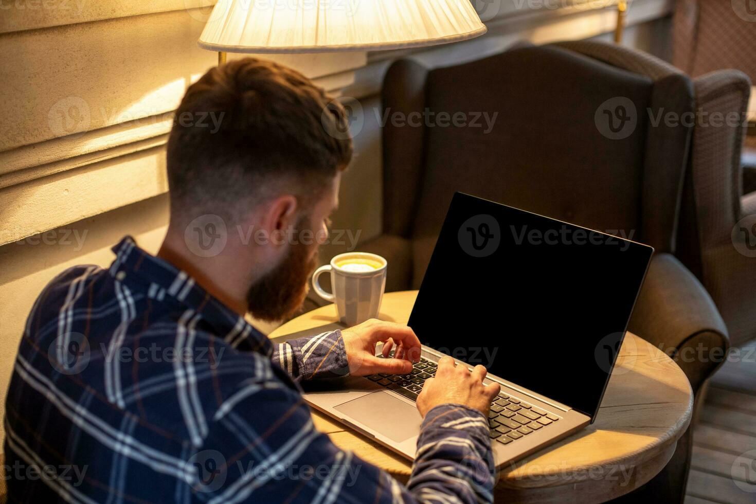 Young man chatting via net-book during work break in coffee shop, male sitting in front open laptop computer with blank copy space screen. photo