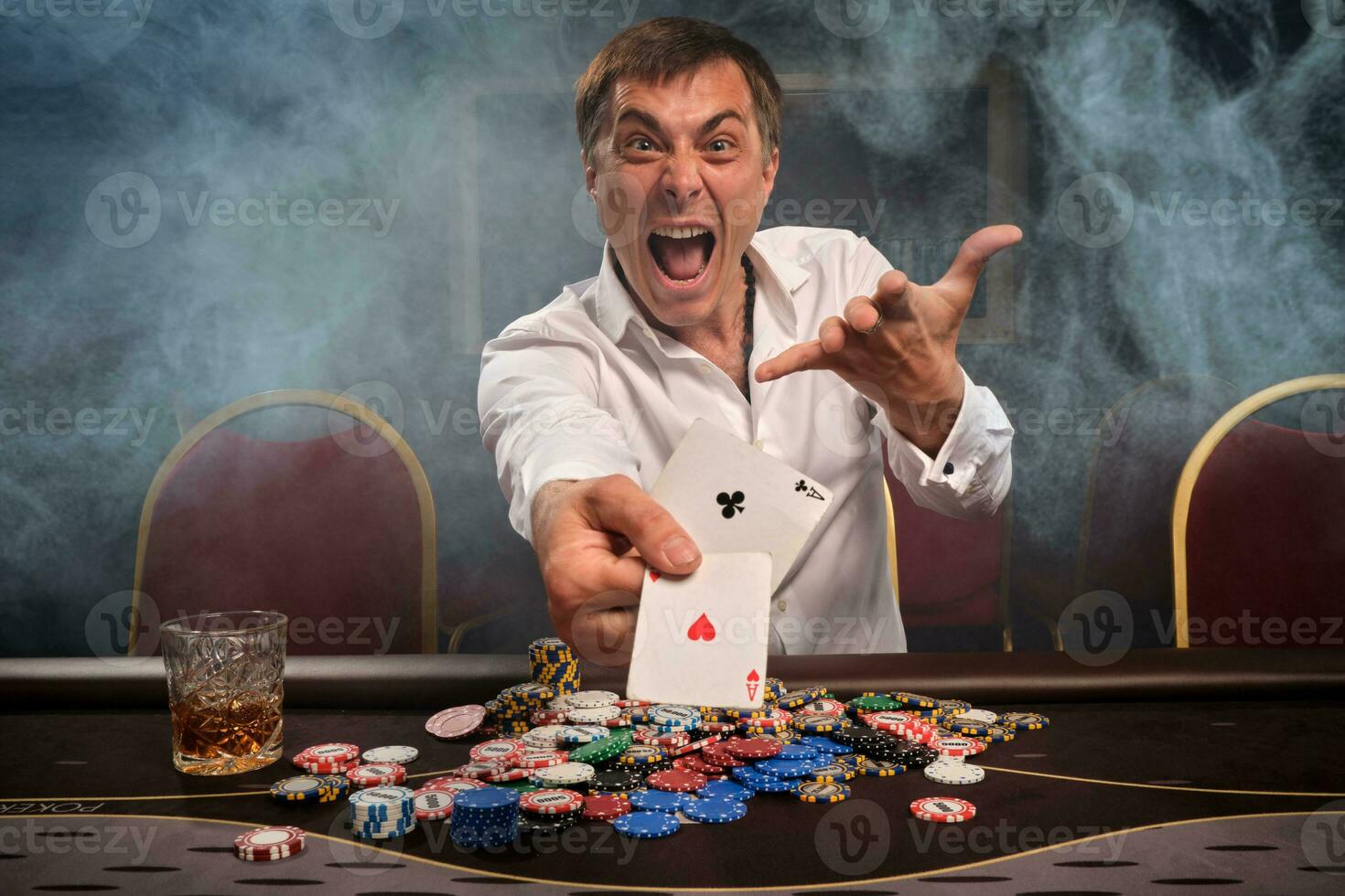 Handsome emotional man is playing poker sitting at the table in casino. photo