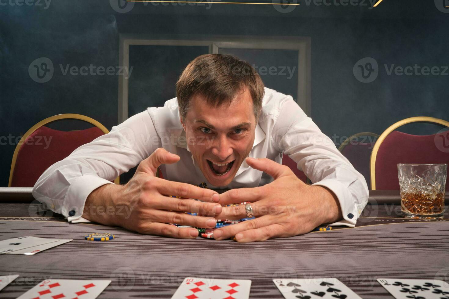 Handsome emotional man is playing poker sitting at the table in casino. photo