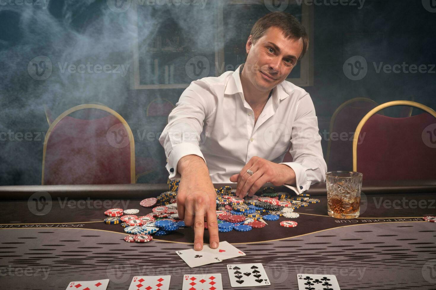 Handsome emotional man is playing poker sitting at the table in casino. photo