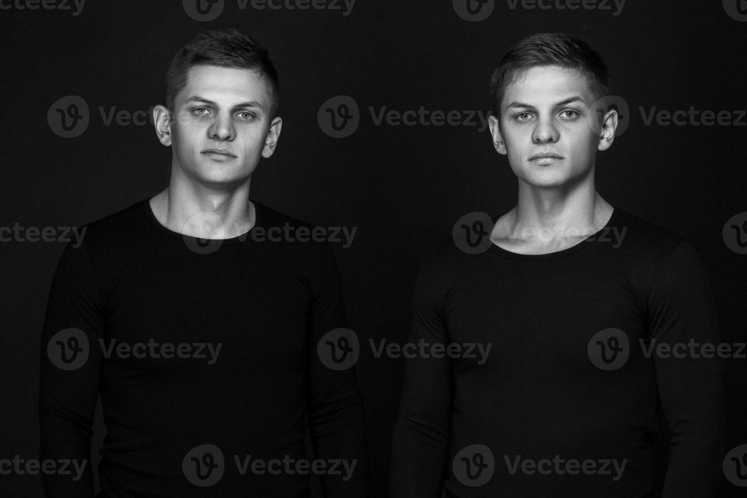 Two attractive positive young twin brothers standing dressed in photo