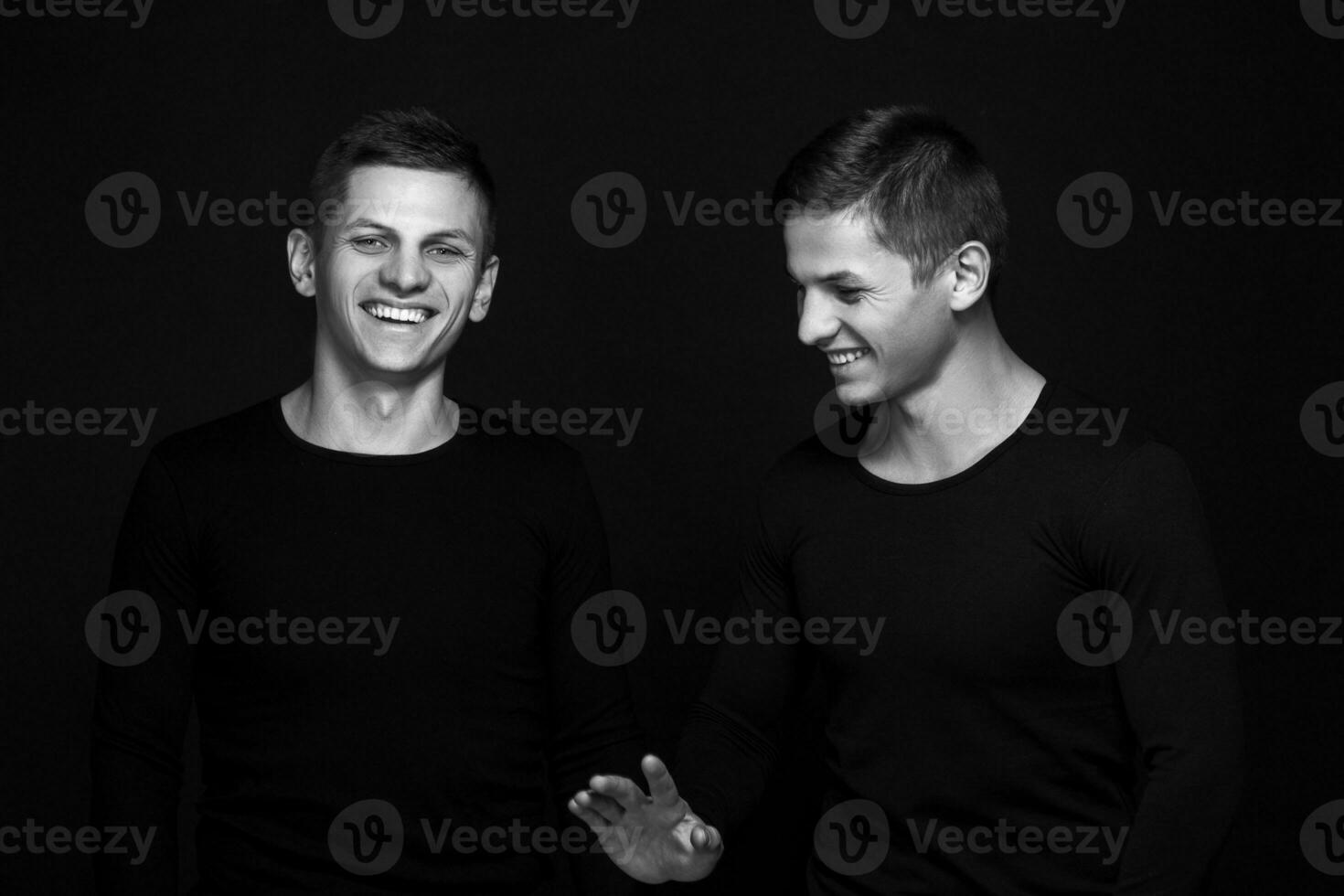 Two attractive positive young twin brothers standing dressed in photo