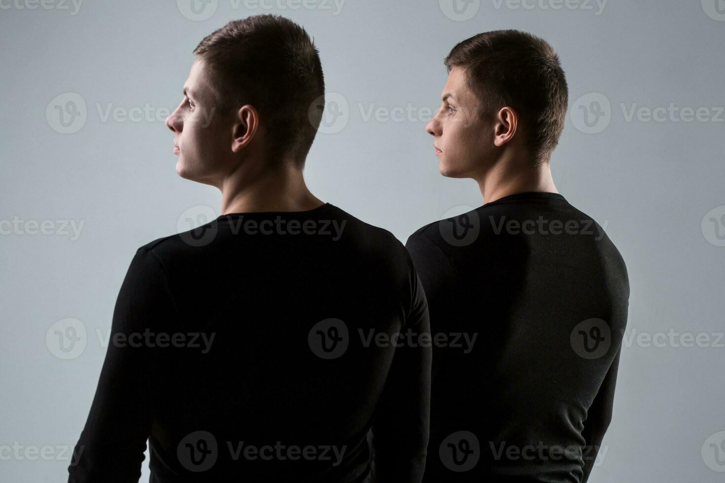 The two twin brother stand with their backs on the gray backgrou photo