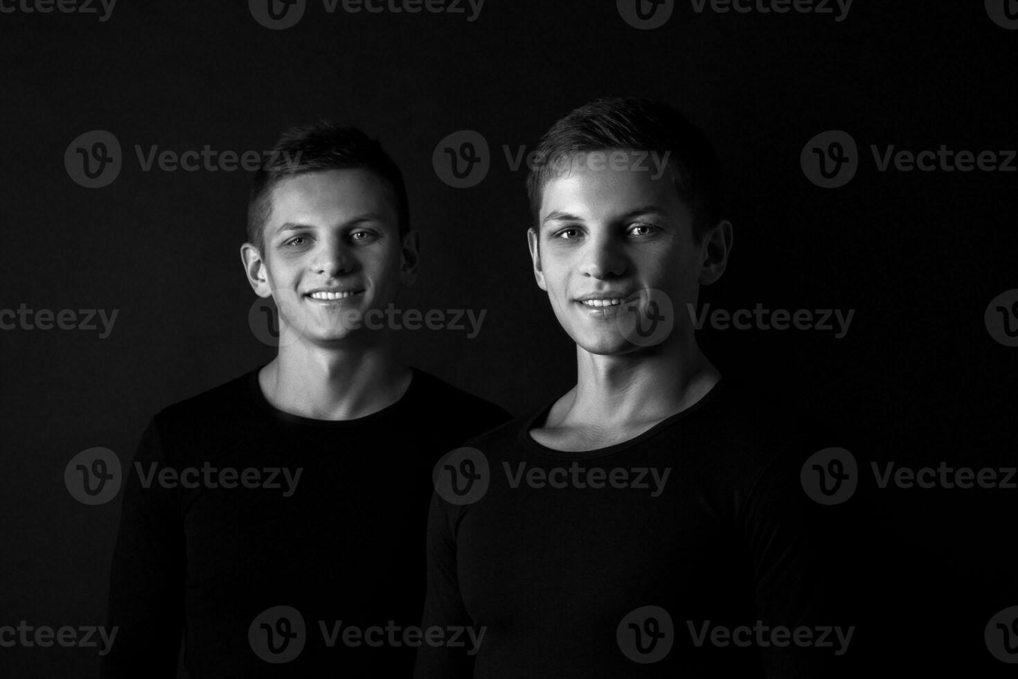 Two attractive positive young twin brothers standing dressed in photo