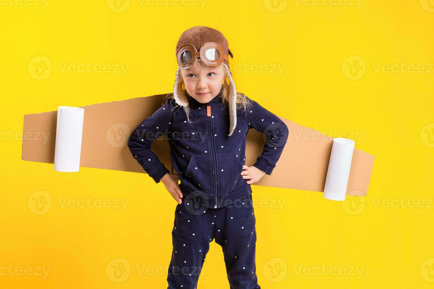 Freedom, girl playing to be airplane pilot, funny little girl with aviator cap and glasses, carries wings made of brown cardboard as an airplane photo