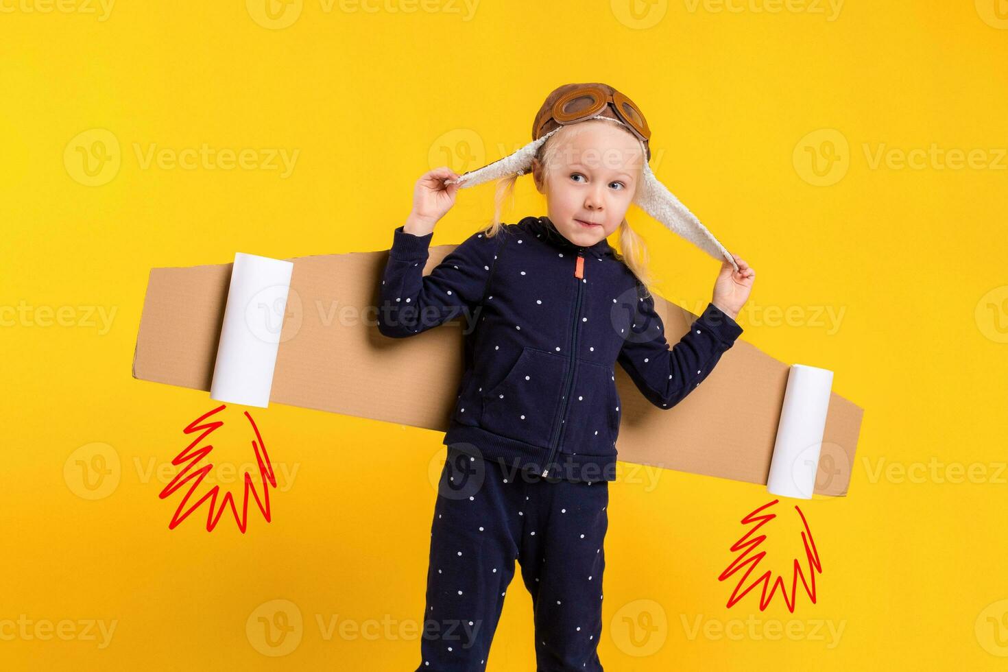 Freedom, girl playing to be airplane pilot, funny little girl with aviator cap and glasses, carries wings made of brown cardboard as an airplane photo