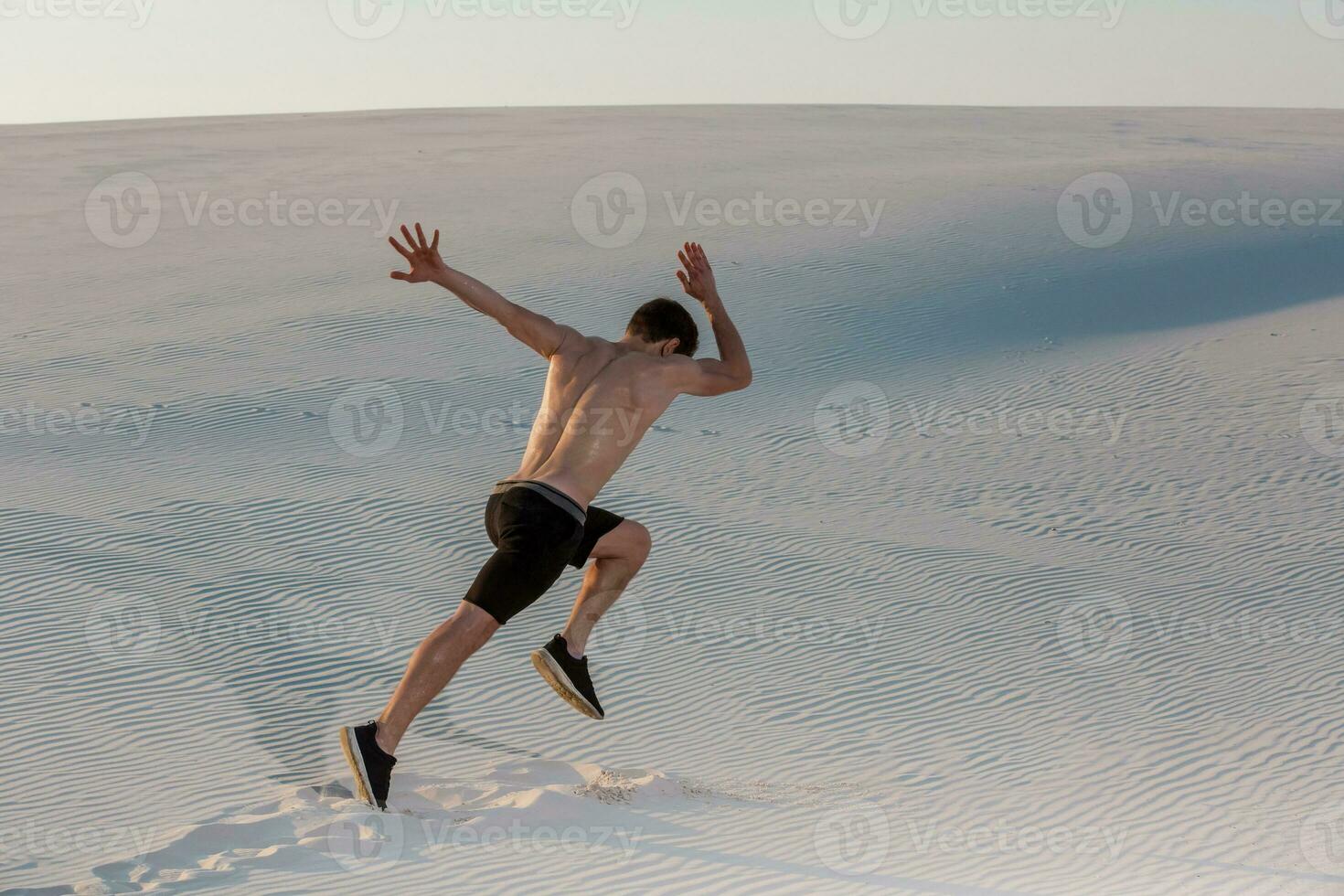 Fit man running fast on the sand. Powerful runner training outdoor on summer. photo