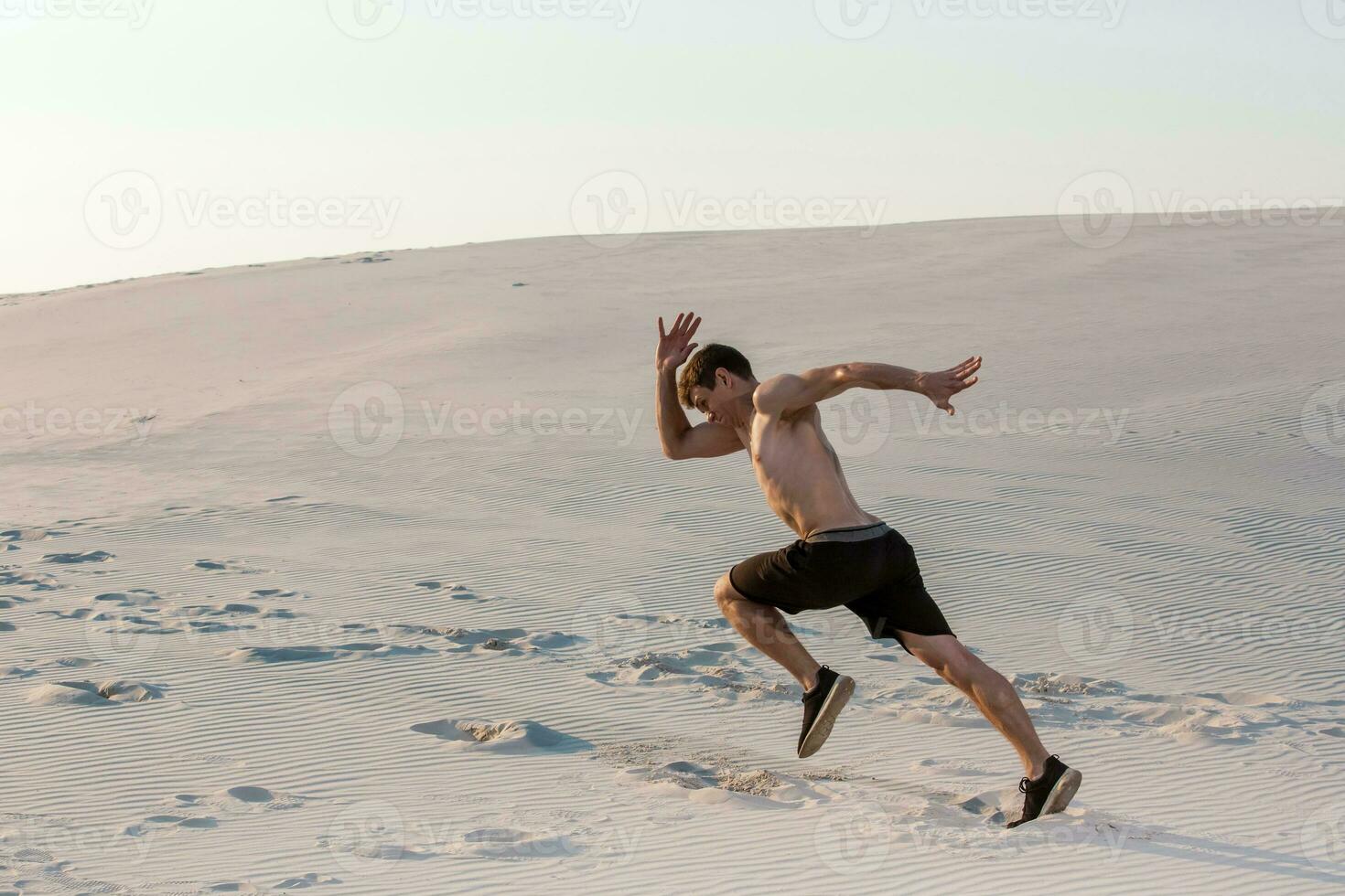 Fit man running fast on the sand. Powerful runner training outdoor on summer. photo