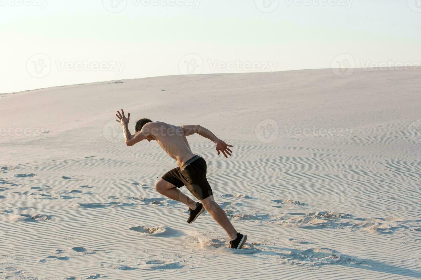 Fit man running fast on the sand. Powerful runner training outdoor on summer. photo