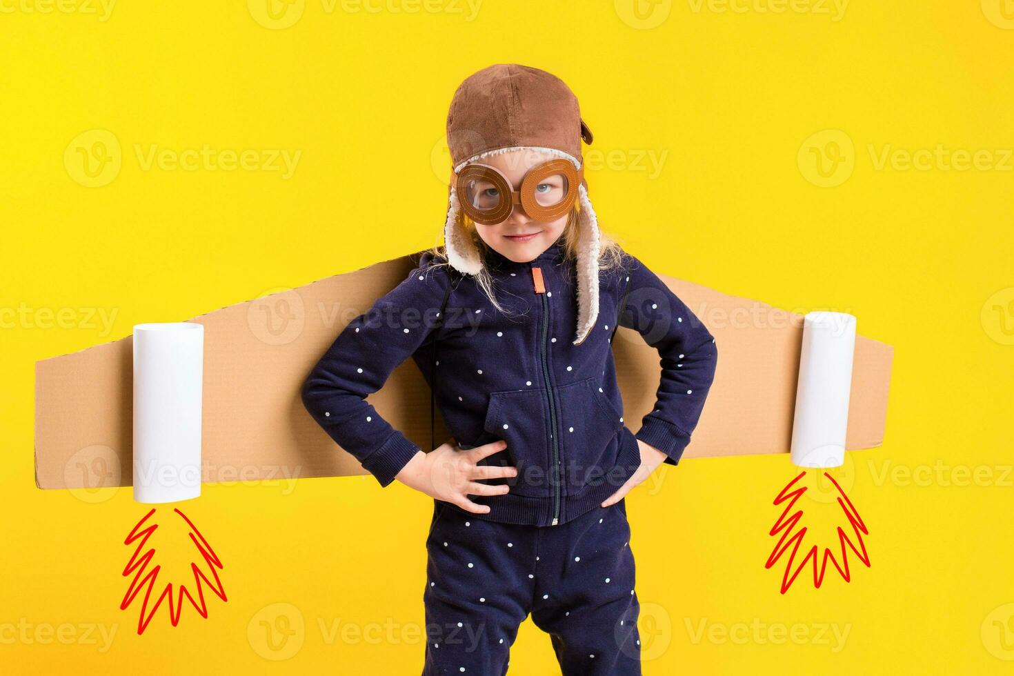 Freedom, girl playing to be airplane pilot, funny little girl with aviator cap and glasses, carries wings made of brown cardboard as an airplane photo