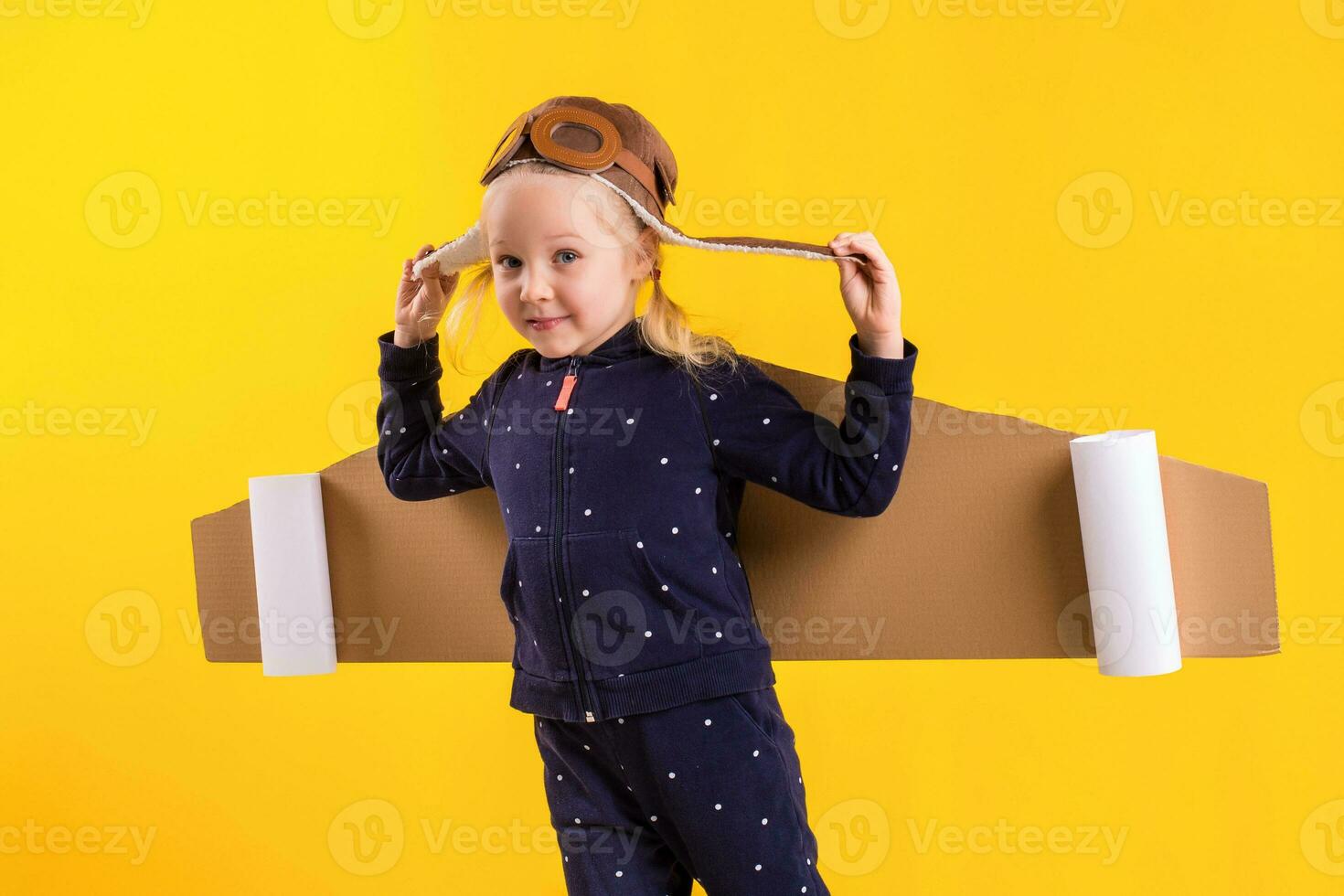 Freedom, girl playing to be airplane pilot, funny little girl with aviator cap and glasses, carries wings made of brown cardboard as an airplane photo