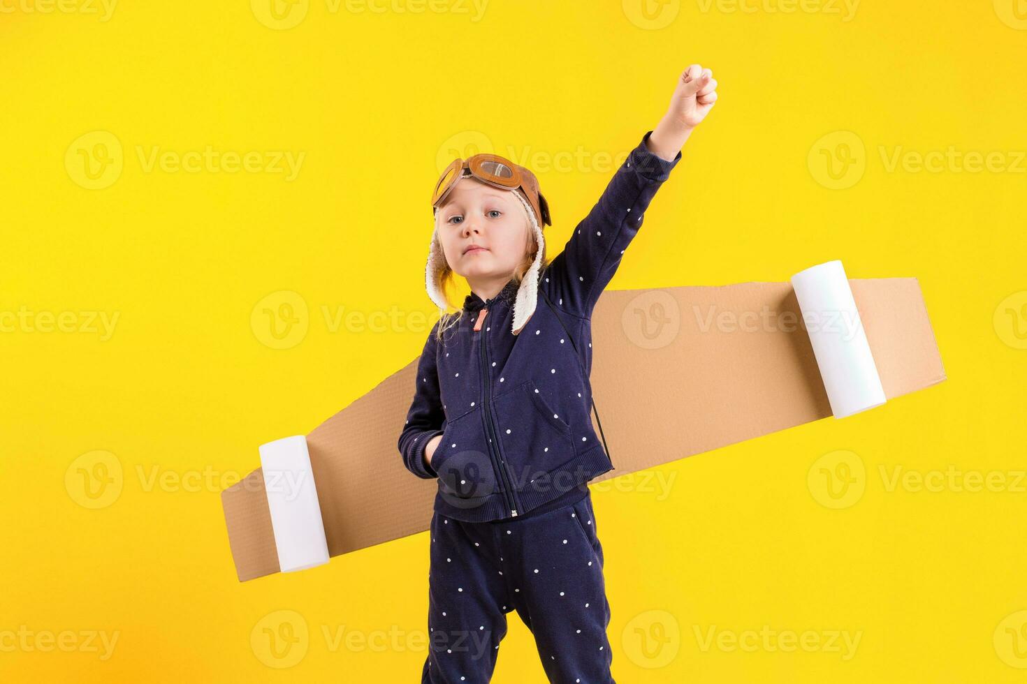 Freedom, girl playing to be airplane pilot, funny little girl with aviator cap and glasses, carries wings made of brown cardboard as an airplane photo