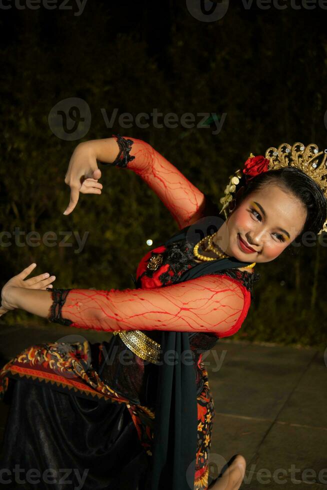 an Asian dancer dancing on her knees while wearing a black and luxurious costume in front of the audience photo