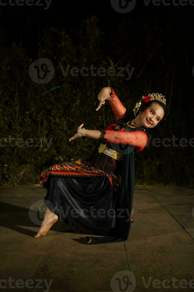 an Asian dancer dancing on her knees while wearing a black and luxurious costume in front of the audience photo