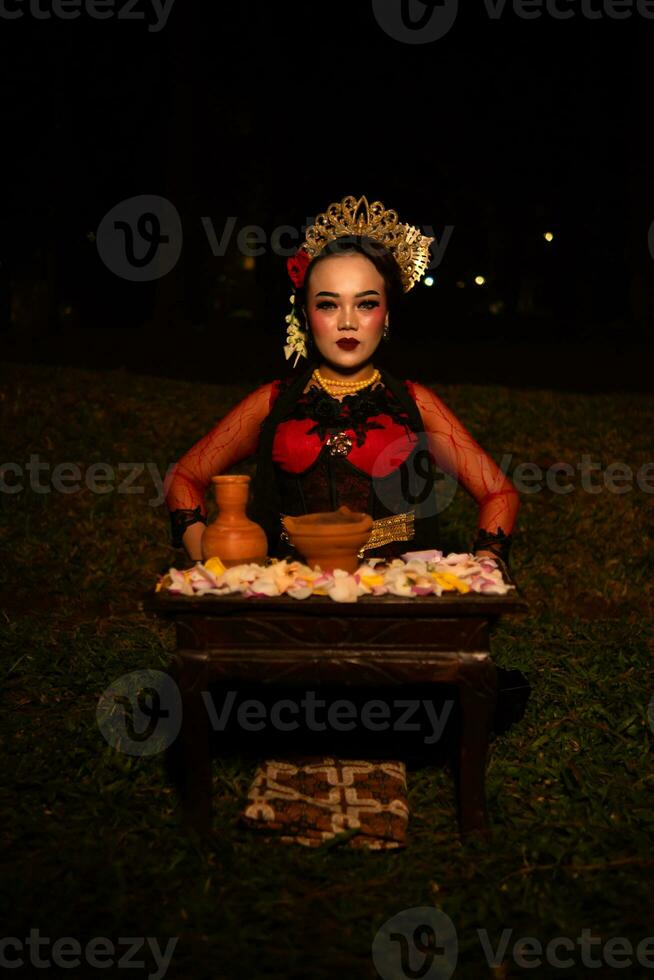 amplio Disparo de un asiático niña en tradicional ropa sentado en un bosque con un mesa lleno de flores foto