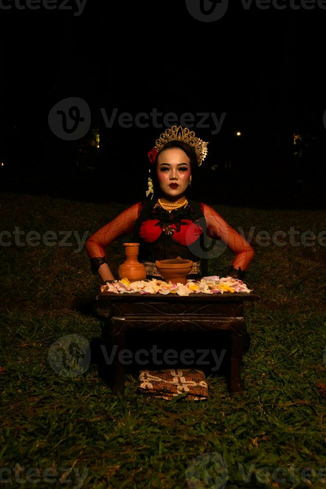 wide shot of an Asian girl in traditional clothes sitting in a forest with a table full of flowers photo