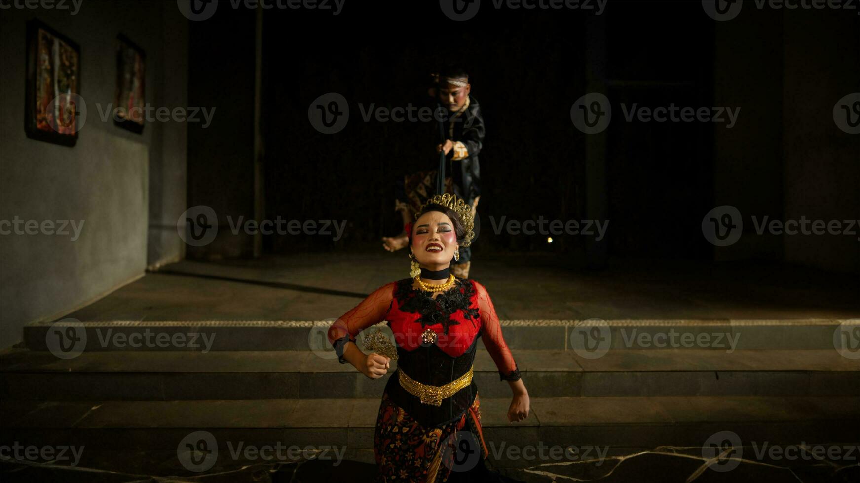 A woman in a red dress tripped and fell in front of a man in a black dress on a staircase photo