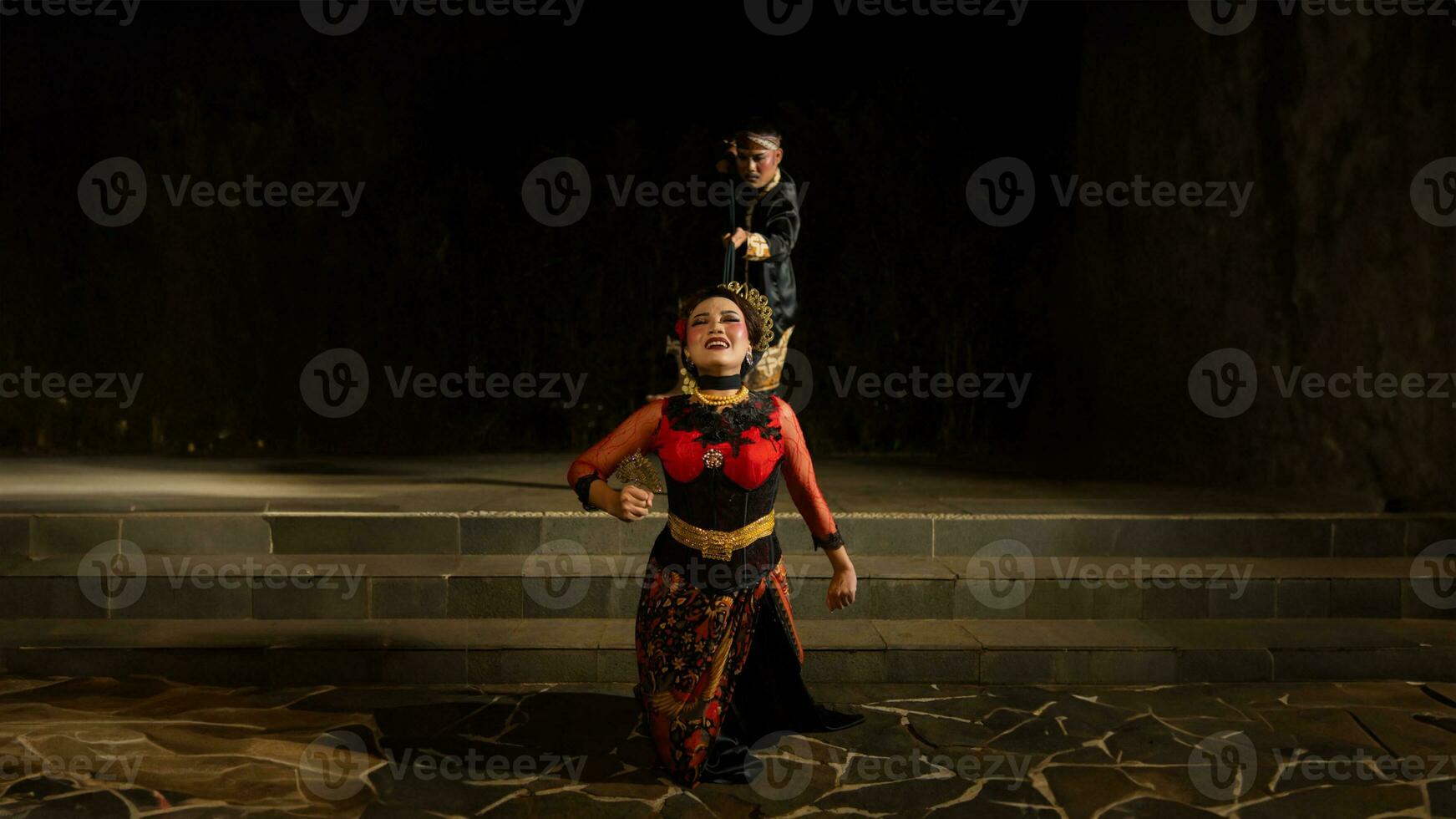 A woman in a red dress tripped and fell in front of a man in a black dress on a staircase photo