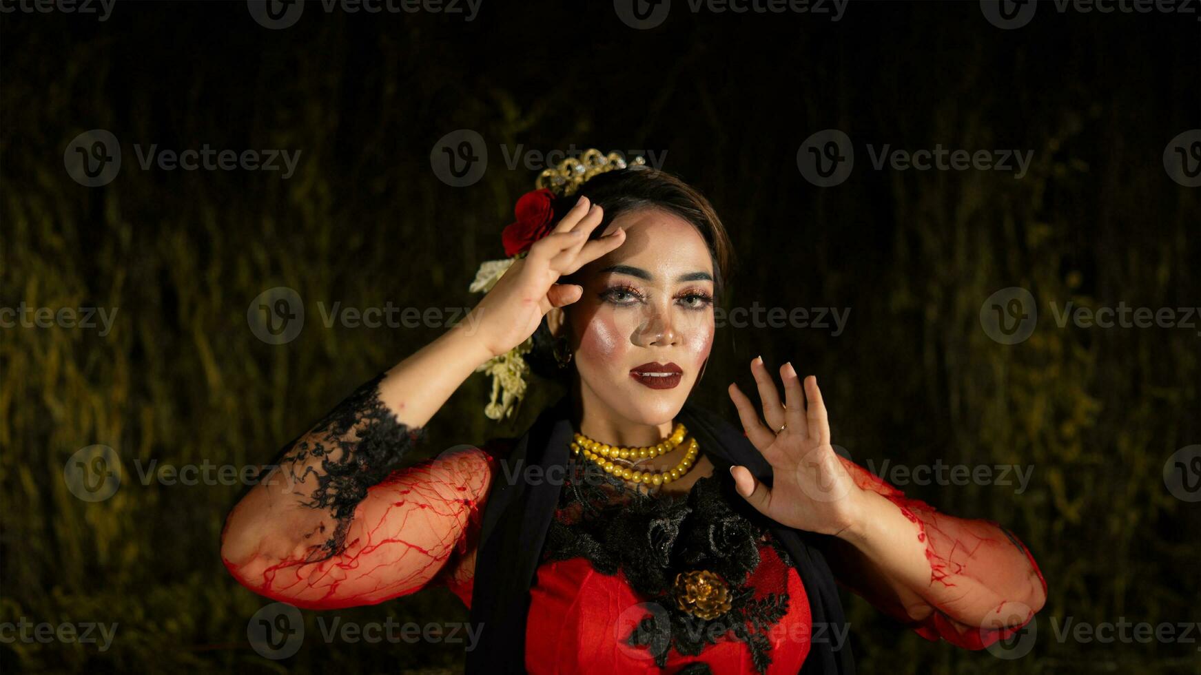 a Balinese dancer dances under the stage lights which highlight her red dress and create an elegant visual photo