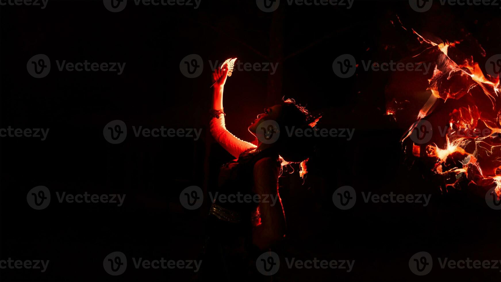 the silhouette of a woman looking at her jewelry with a face full of sadness and the fire burning around her photo