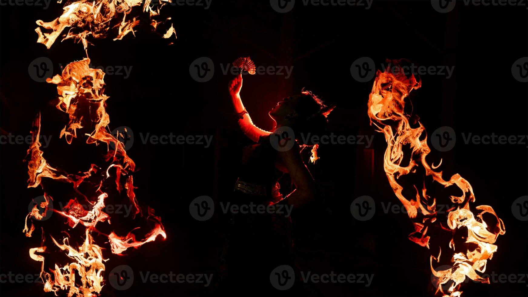 the silhouette of a female dancer holding sparkling jewelry and looking sharp in the dark with fire burning in the background photo